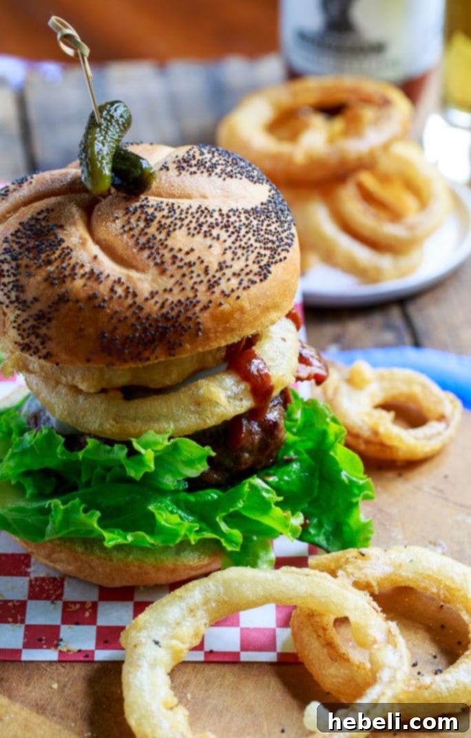 Close-up of a Cowboy Burger, showcasing the melted cheese, crispy bacon, and golden onion rings.