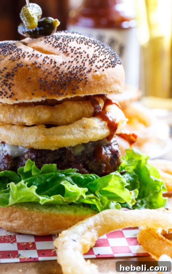 Close-up of a Cowboy Burger, showcasing the intricate layers of bacon, onion rings, and Stubb's BBQ sauce.