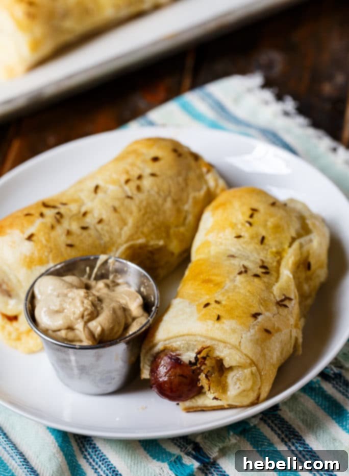 Close-up shot of a single Brats in a Blanket, showing the golden-brown puff pastry, a glimpse of the bratwurst, and melted cheese, ready for serving.