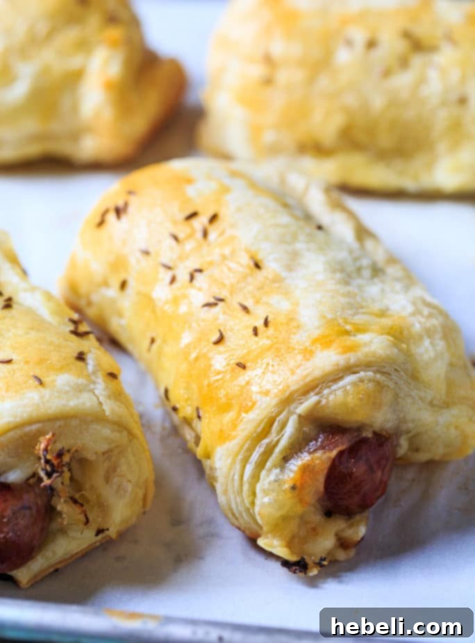 A close-up of a Brats in a Blanket, showing the flaky pastry and golden brown finish, with a blurred background.