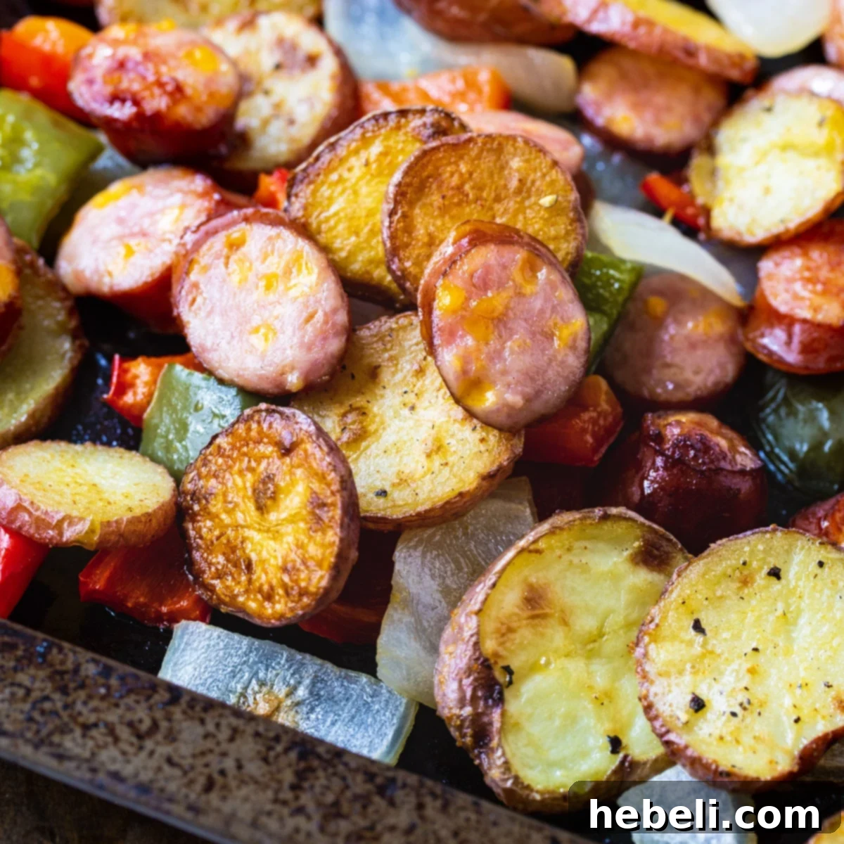 A close-up shot of golden brown Oven-Roasted Sausage and Potatoes on a baking sheet, showcasing crispy edges and vibrant vegetables.