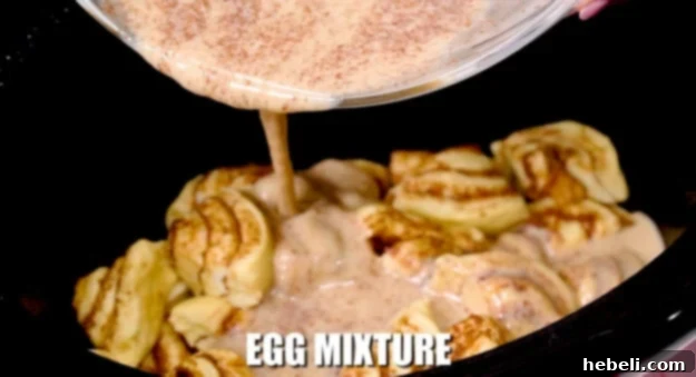 Pouring the liquid egg mixture over the cinnamon roll pieces in the slow cooker.