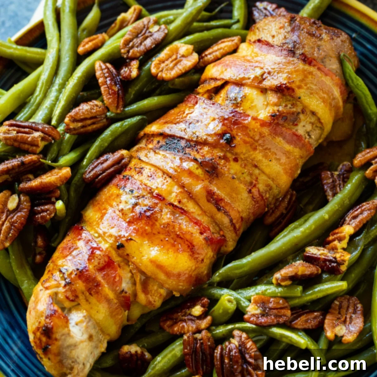 A perfectly cooked Bacon-Wrapped Pork Tenderloin, sliced and served on a plate with vibrant green beans, ready to be enjoyed.