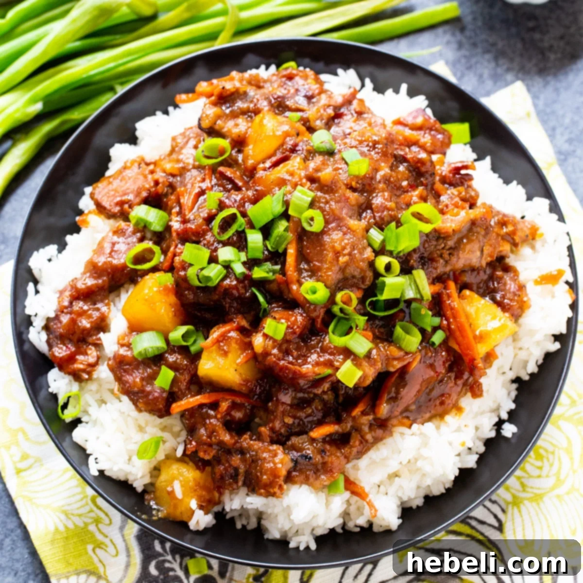 Delicious Slow Cooker Spicy Mongolian Beef with Pineapple served over fluffy white rice, garnished with fresh green onions.