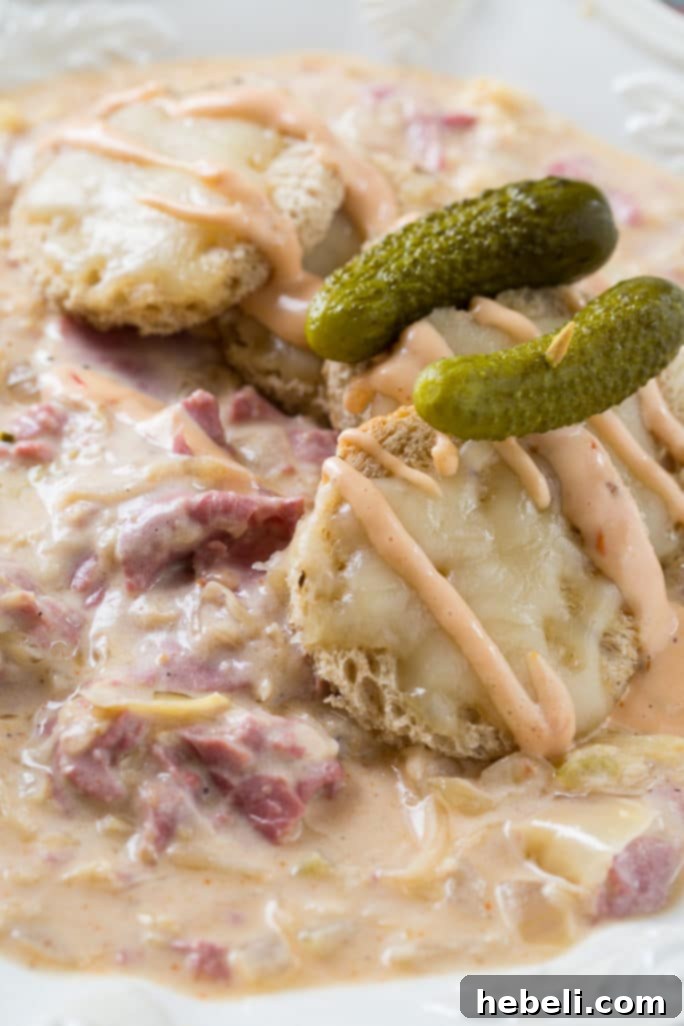 Two bowls of Reuben Soup ready to be served, garnished with melted cheese and rye bread.