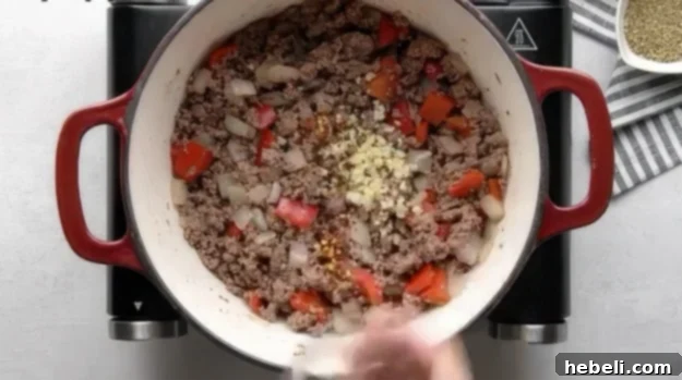 Adding minced garlic and red pepper flakes to the browned ground beef mixture.