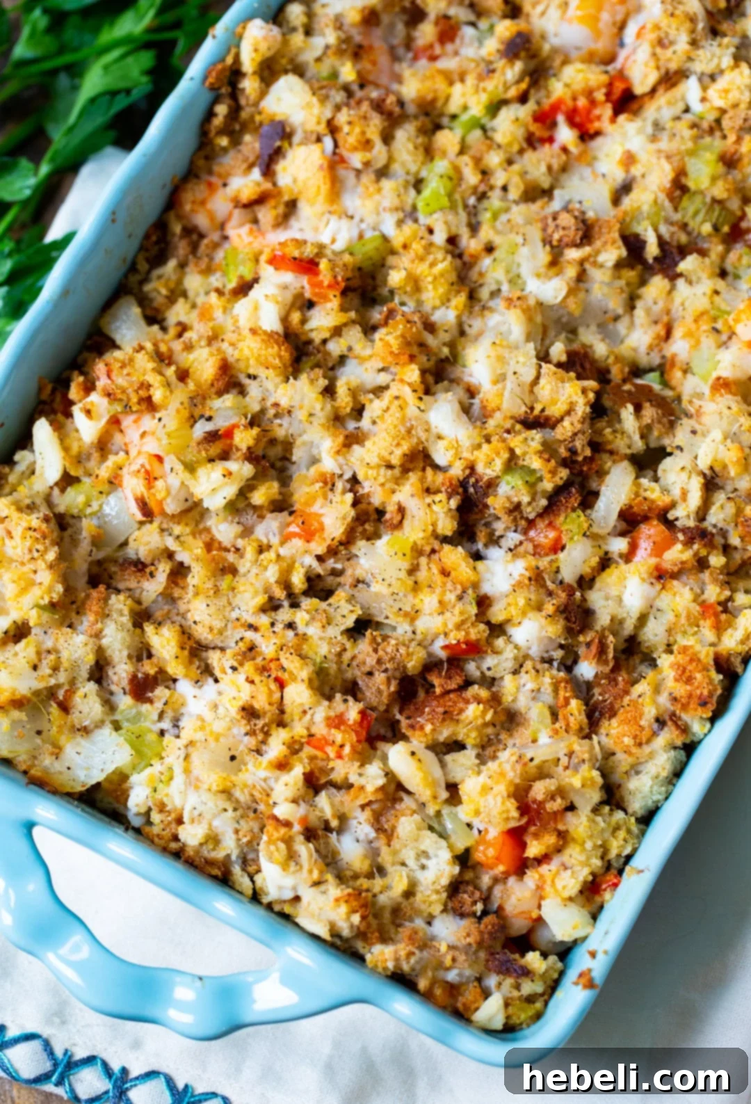 A close-up shot of golden-brown Savannah Seafood Stuffing baking in a vibrant blue casserole dish, showcasing its inviting crust and steamy interior.