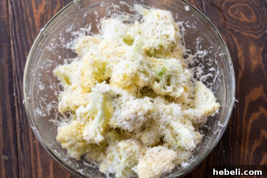 Cauliflower florets mixed with olive oil, garlic, and cayenne pepper in a bowl, before adding Parmesan.