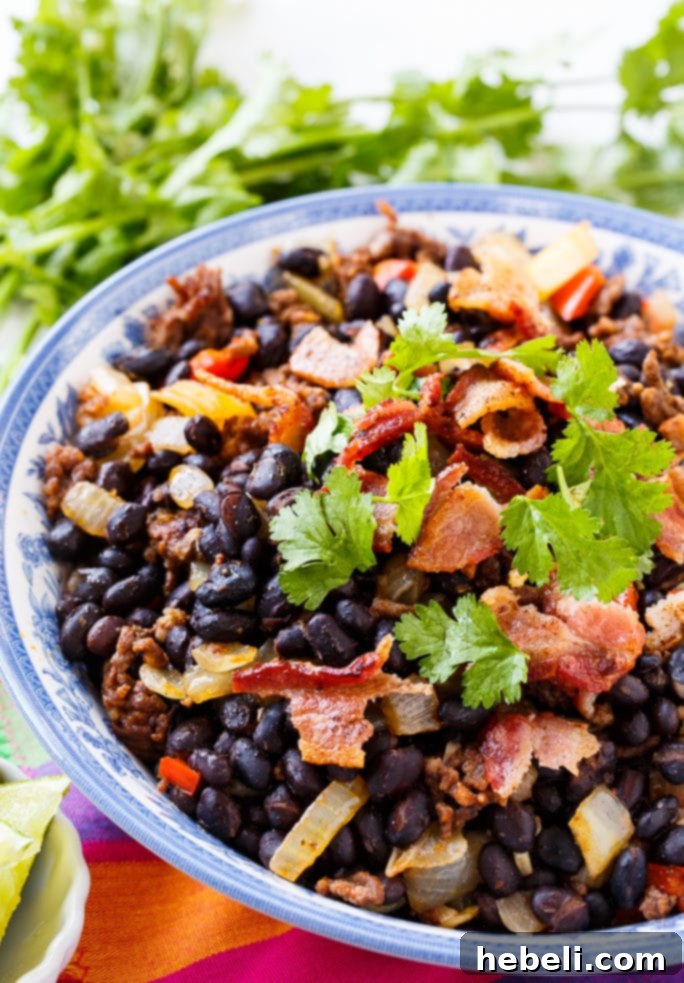 A close-up shot of Chorizo Black Beans, garnished with vibrant fresh cilantro and crispy crumbled bacon, showcasing their delicious texture.