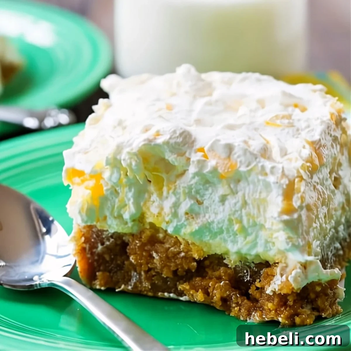 A perfectly portioned slice of Pineapple Delight on a small white plate, showcasing its distinct layers: golden graham cracker crust, creamy yellow filling, and fluffy white topping.