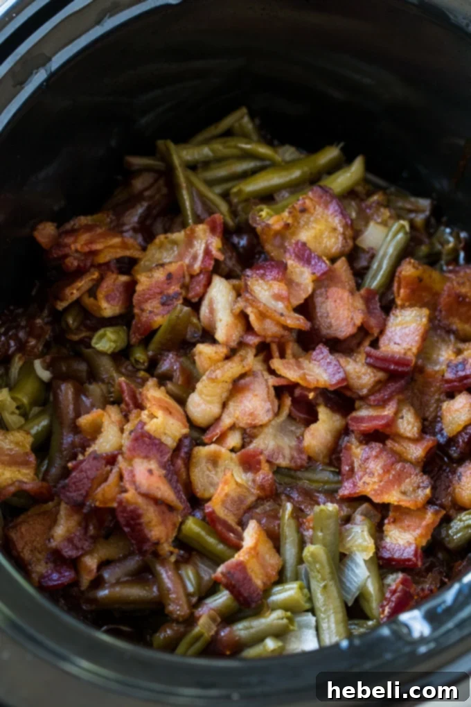 A close-up of Slow Cooker Barbecued Green Beans, glistening with sauce and topped with generous amounts of bacon.
