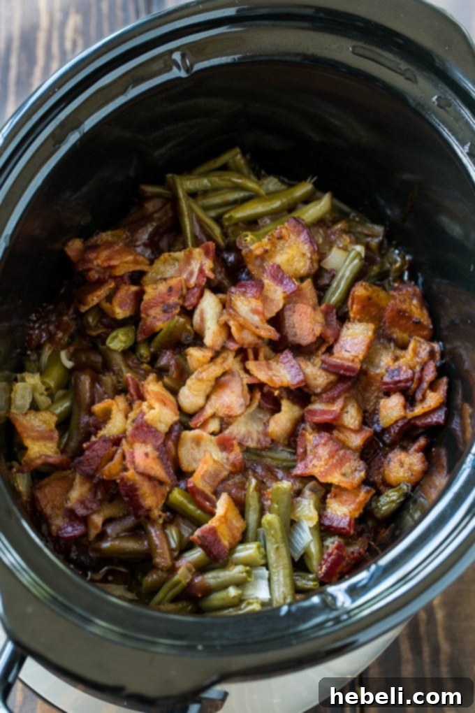 A slow cooker filled with BBQ Green Beans, simmering gently, with onions and bacon visible.