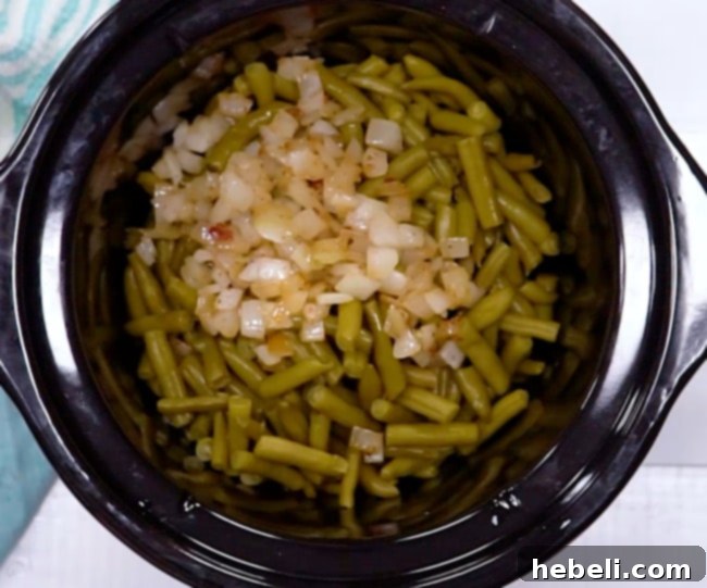 Sautéed onions being added on top of green beans in a slow cooker.
