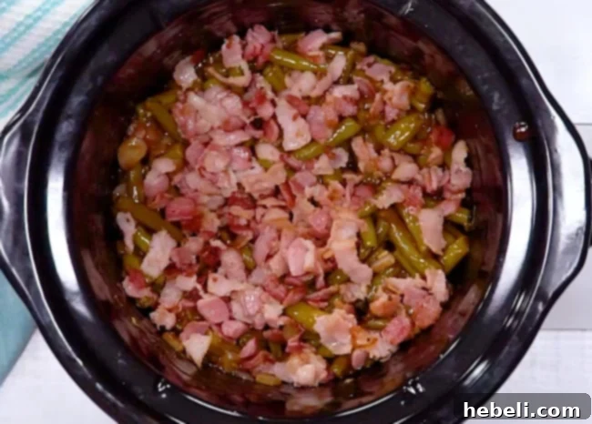 Crispy bacon bits sprinkled over the top of green beans and sauce in a slow cooker, ready for cooking.
