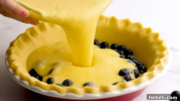 Pouring pie batter into the crust over blueberries.