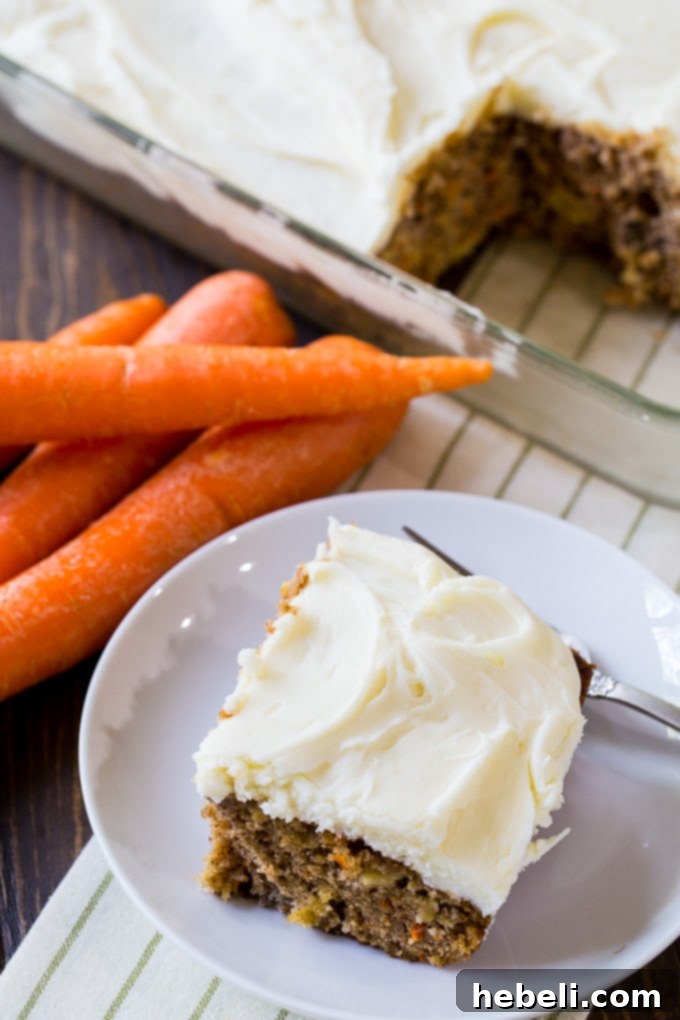 A close-up of a slice of Pineapple Carrot Cake topped with rich cream cheese frosting