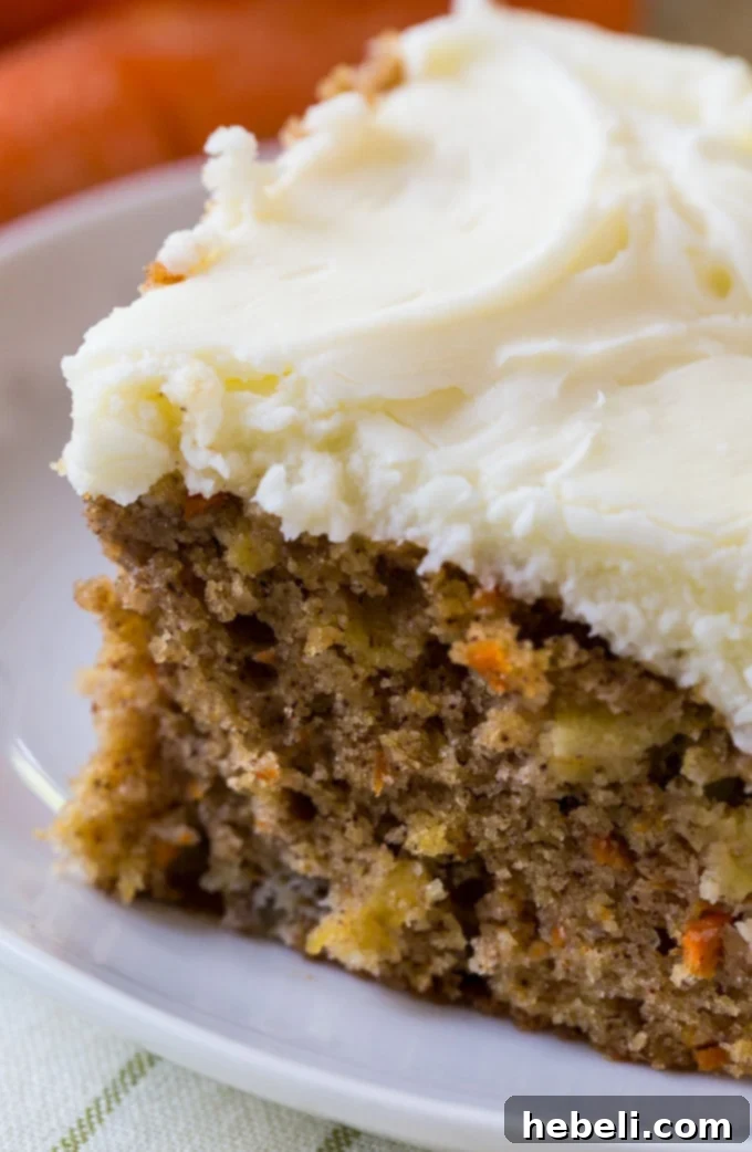 Close-up of a slice of Pineapple Carrot Cake with visible carrots, pineapple bits, and thick cream cheese frosting