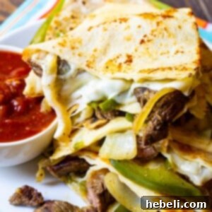 Triangles of Philly Cheese Steak Quesadilla piled up on plate with bowl of salsa.