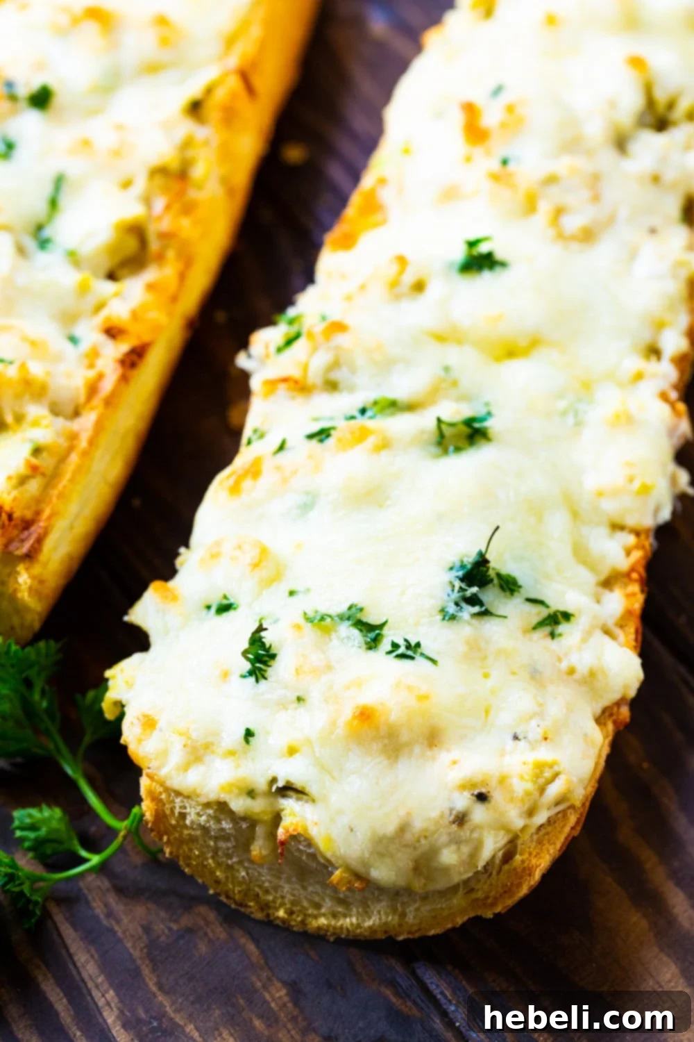 Long loaf of French bread generously topped with cheesy artichoke crab mixture, ready for baking.