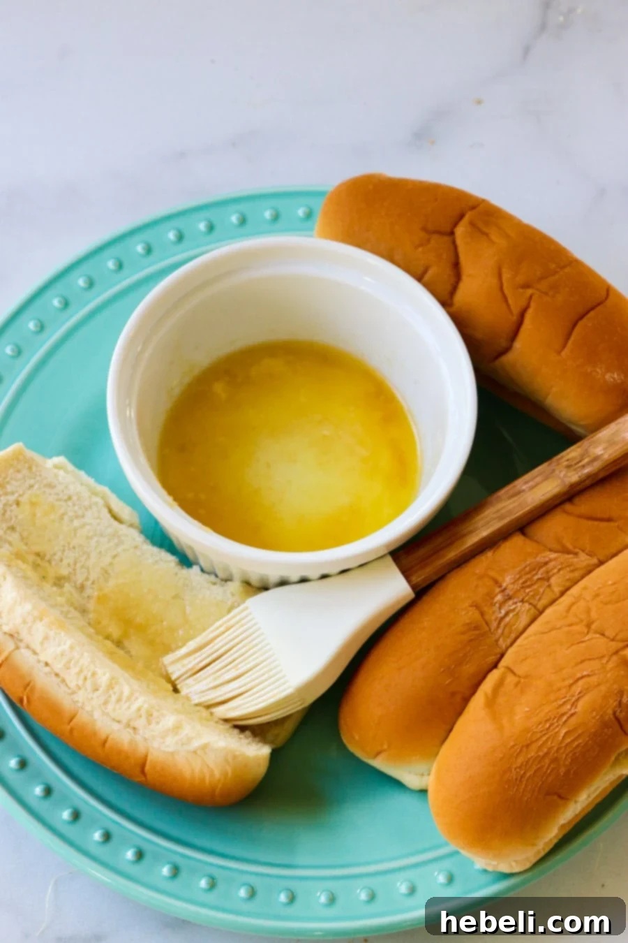 Cheesy Frank Melt 4 Hot dog buns being brushed with melted garlic butter on a cutting board.