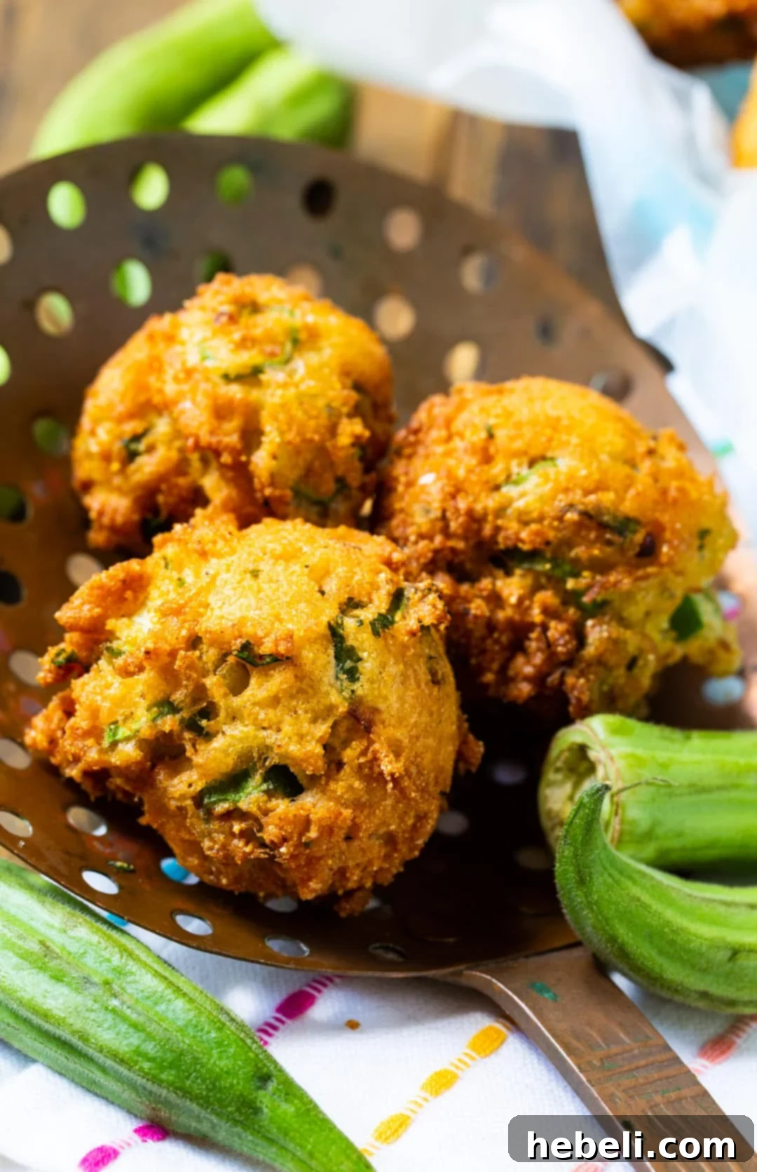 Southern Okra Hushpuppies 3 Three perfectly golden-brown Okra Hush Puppies gracefully resting on a metal straining spoon, fresh out of the hot oil.