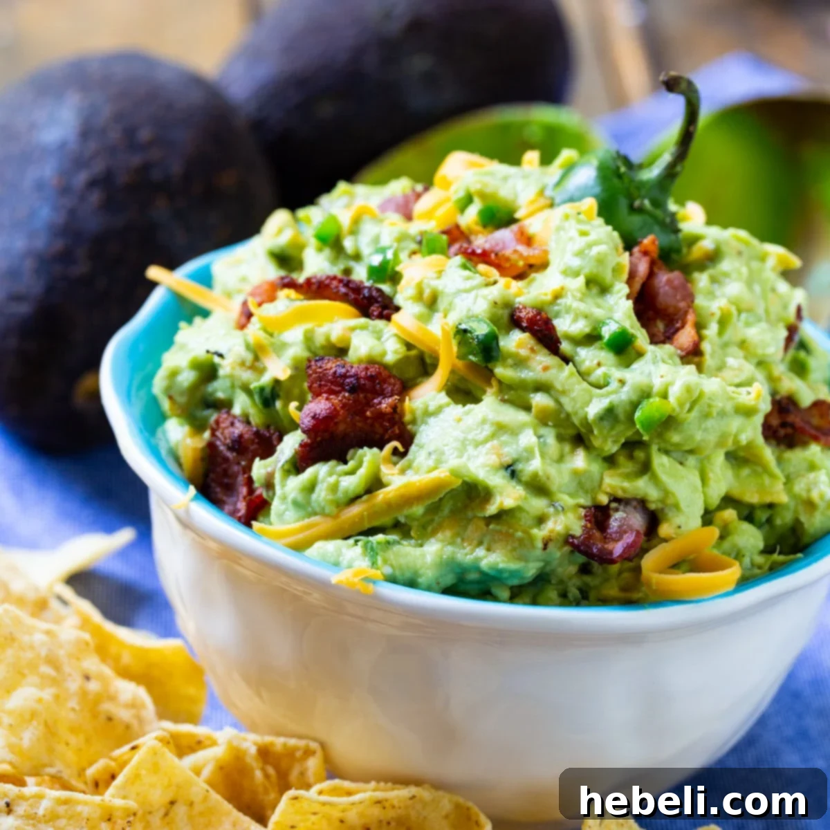 A bowl of creamy Jalapeno Popper Guacamole surrounded by crispy tortilla chips, ready for dipping.