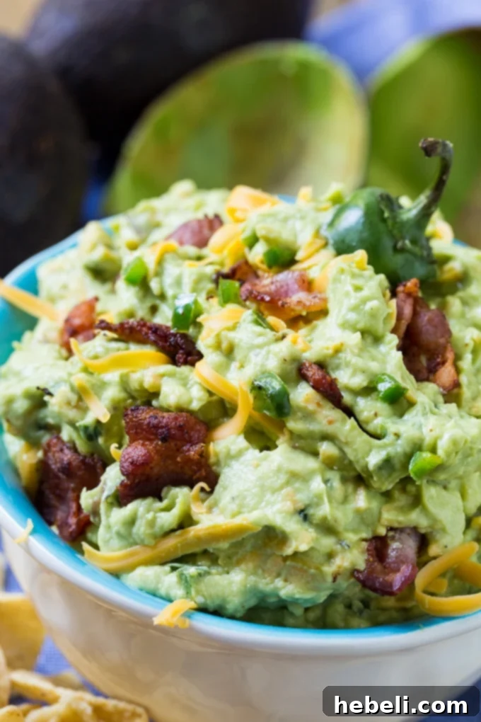 A top-down view of a large serving bowl filled with Jalapeno Popper Guacamole, showcasing its creamy texture and the colorful bits of bacon, cheese, and jalapeño. Ready for a party.