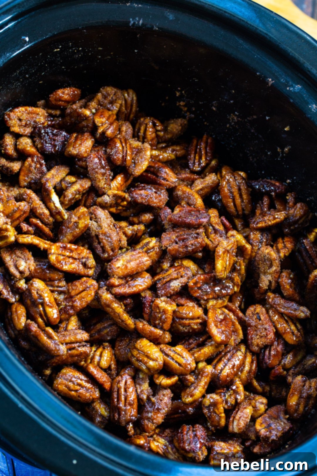 Candied Pecans gently simmering in a slow cooker, covered in a sweet, sugary glaze.