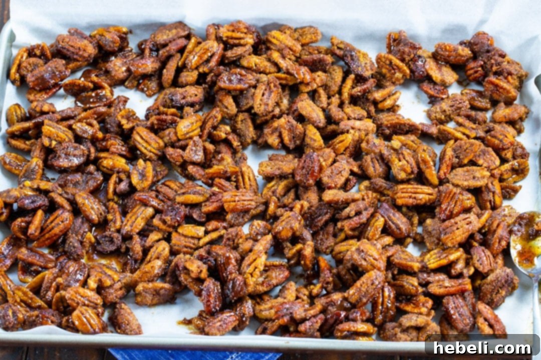 Freshly cooked candied pecans spread out on a sheet of parchment paper, cooling and hardening.