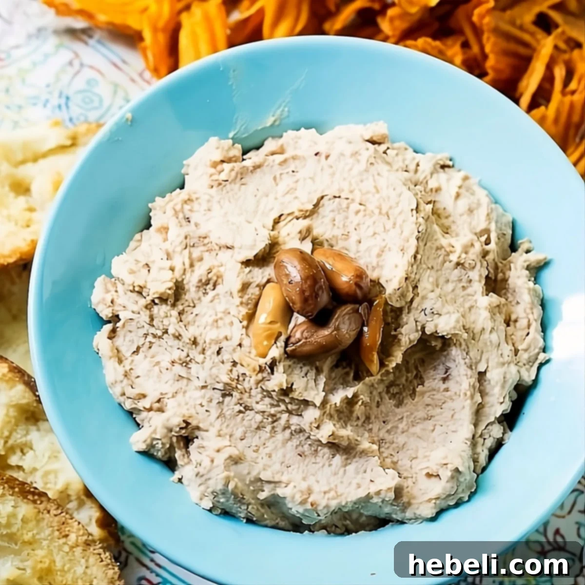 Fiery Boiled Peanut Dip 2 Spicy Boiled Peanut Hummus in a vibrant blue bowl, surrounded by golden sweet potato chips, ready for a delicious snack or party spread.