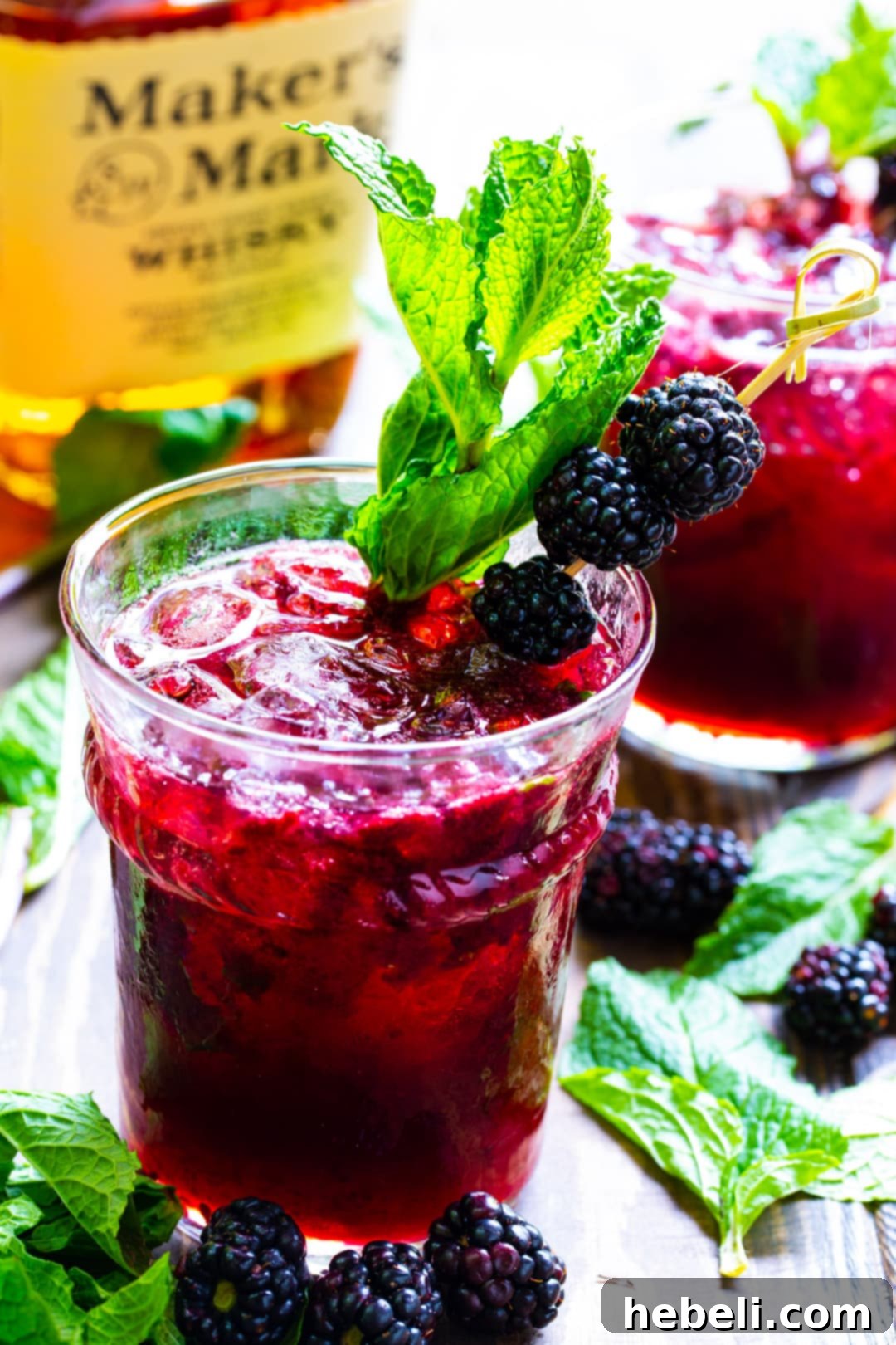 Blackberry Mint Julep Delights 3 A single Blackberry Mint Julep in a glass, surrounded by loose fresh mint leaves and whole blackberries, emphasizing its natural ingredients.