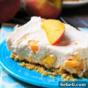 Close-up of a No-Bake Peach Cheesecake Bar, showing the graham cracker crust, creamy peach filling, and fresh peach garnish on a white plate.