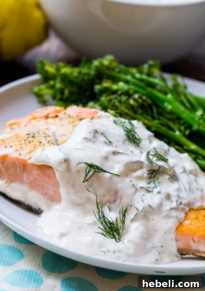 Close-up of baked salmon covered in a creamy dill sauce, garnished with fresh dill sprigs