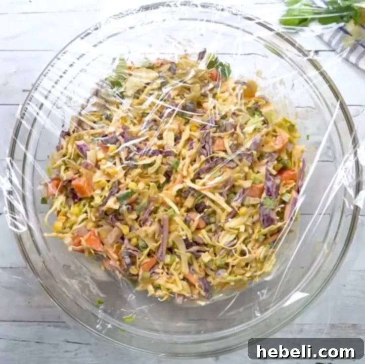 Bowl of Mexican coleslaw covered with plastic wrap, chilling in the refrigerator.