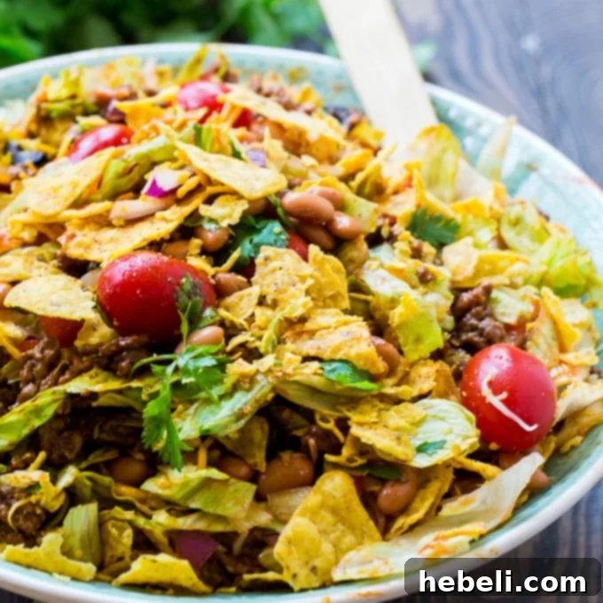 A large bowl of vibrant Dorito Taco Salad, showcasing layers of seasoned beef, fresh vegetables, cheese, and crunchy Doritos.