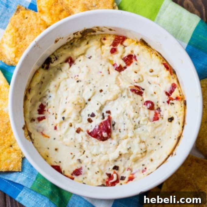 Close-up of a warm, creamy Spicy Feta Cheese Dip, garnished with red pepper flakes and herbs, served with pita chips.