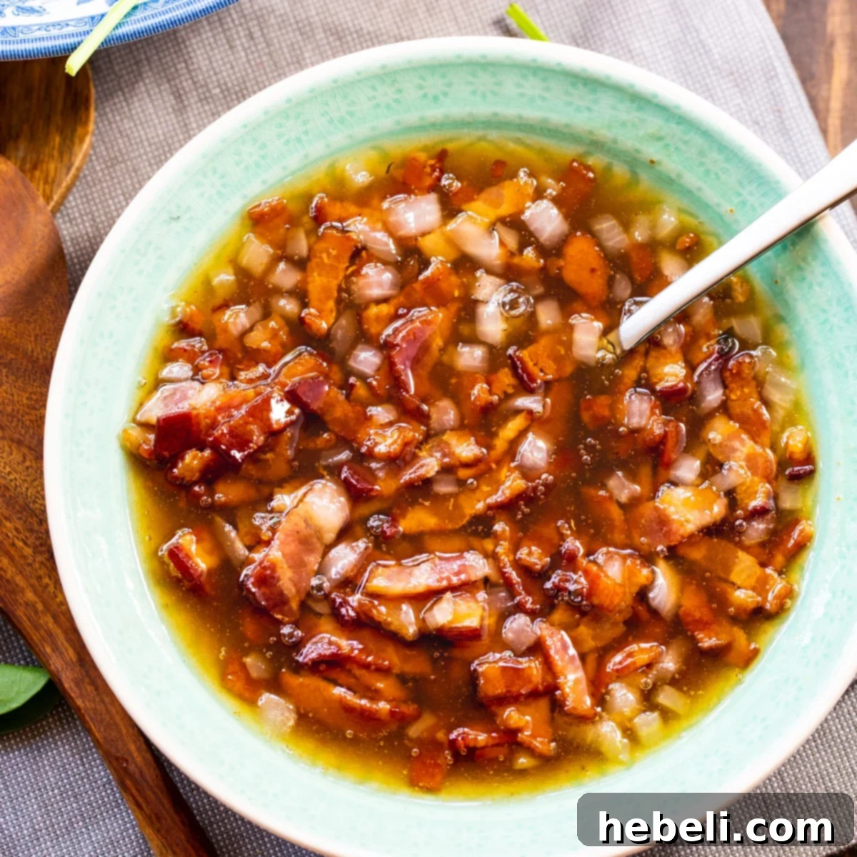 A bowl of freshly made Hot Bacon Dressing, rich in color and texture, with visible crispy bacon bits.