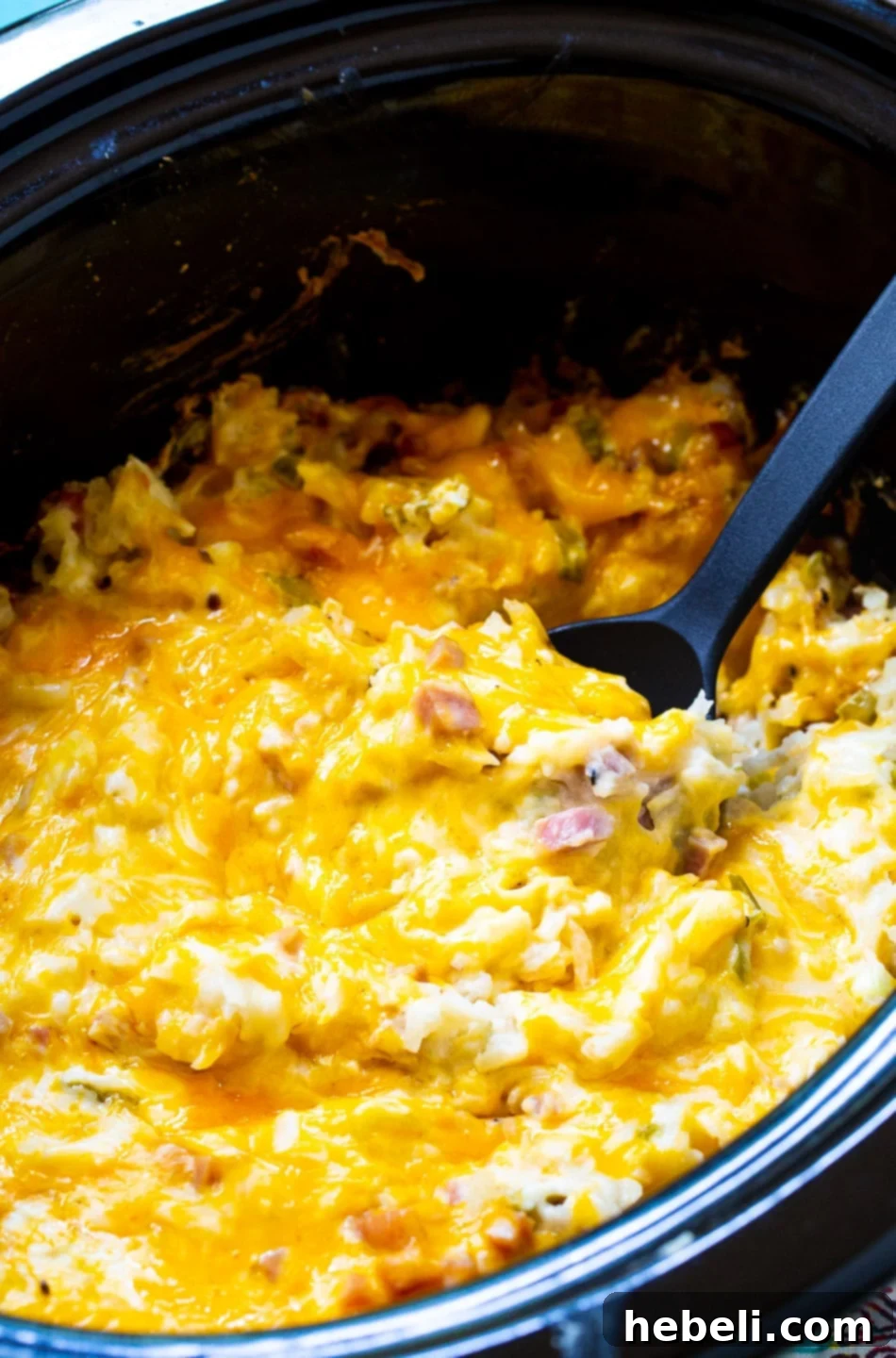 A slow cooker filled with bubbling Ham and Cheese Hash Brown Casserole, showcasing its readiness to serve.