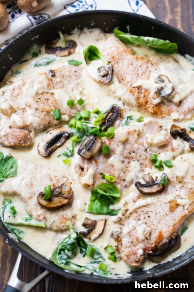 Close-up of Creamy Parmesan Pork Chops adorned with golden-brown sautéed mushrooms and wilted spinach, highlighting the rich texture of the sauce and its vibrant ingredients.
