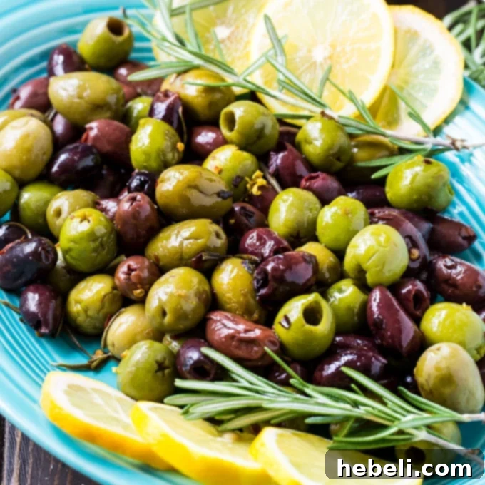 A bowl of warm rosemary olives, garnished with fresh rosemary sprigs and lemon zest.