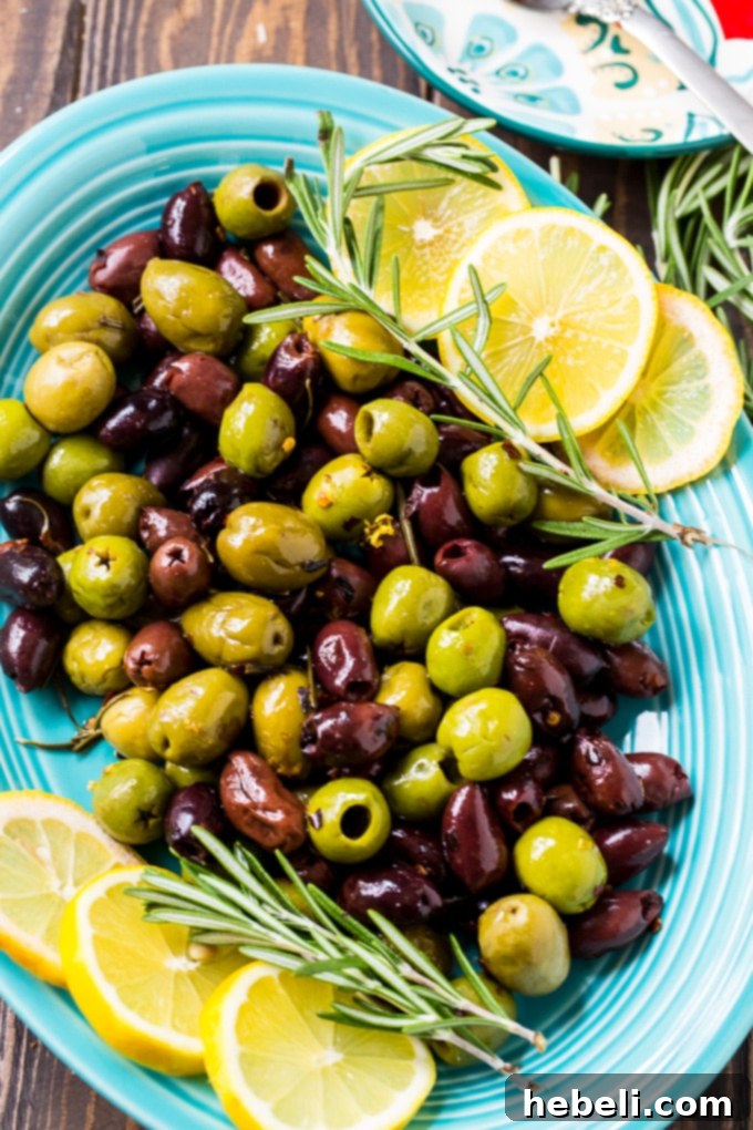 Close-up of freshly baked Warm Rosemary Olives with visible lemon zest, red pepper flakes, and rosemary leaves.