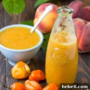 A jar of finished Peach Habanero Hot Sauce on a wooden background, with ingredients blurred in the background.