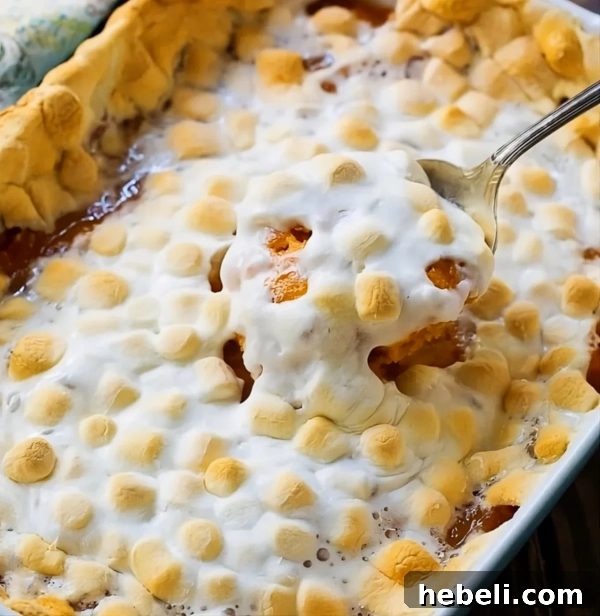 Spoon scooping creamy Sweet Potato Casserole with Marshmallows out of a baking dish, highlighting the golden, gooey topping.