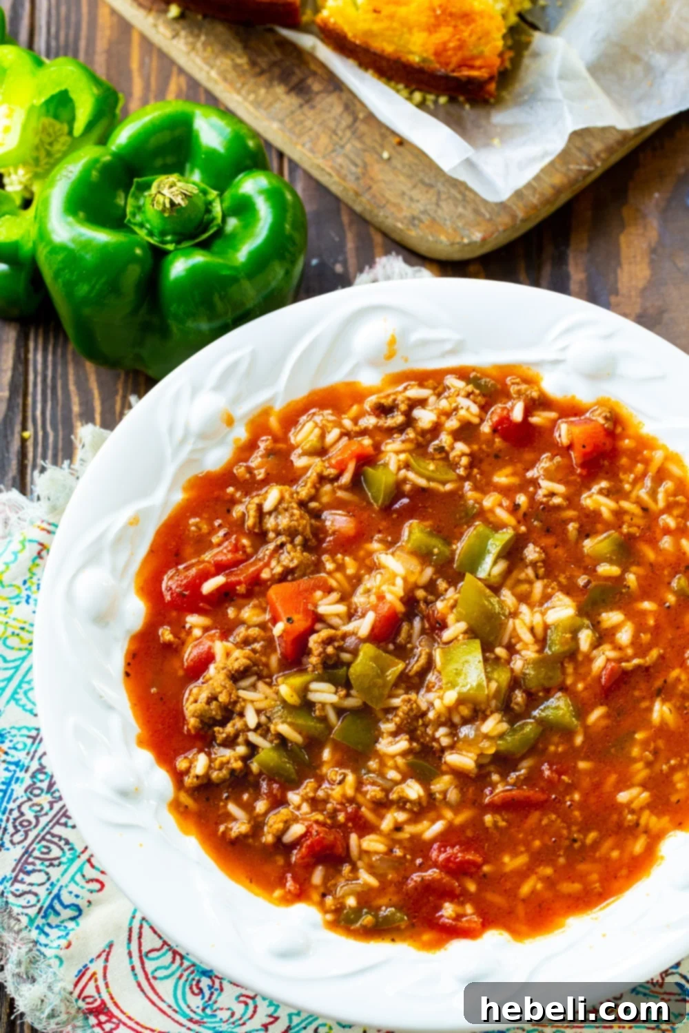 A hearty bowl of Stuffed Pepper Soup garnished with fresh parsley, with green bell peppers on the side.