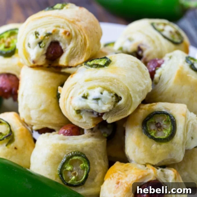 Spicy Piggy Poppers 2 Golden-brown Jalapeno Popper Pigs in a Blanket, fresh from the oven, garnished with a slice of fresh jalapeño.