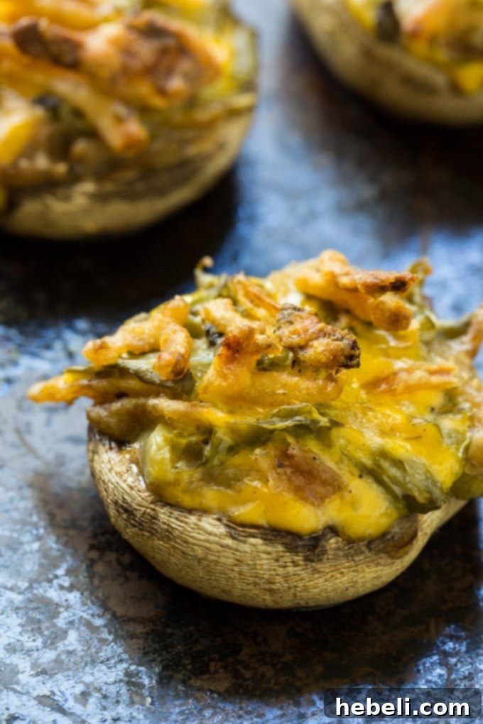 Green Bean Casserole Mushroom Bites 3 Close-up shot of two perfectly baked Green Bean Casserole Stuffed Mushrooms on a white plate, showcasing their golden-brown tops and creamy filling