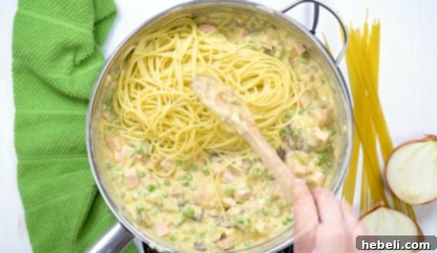 Drained spaghetti being added to the creamy ham and cheese sauce in the skillet, ready to be tossed together.