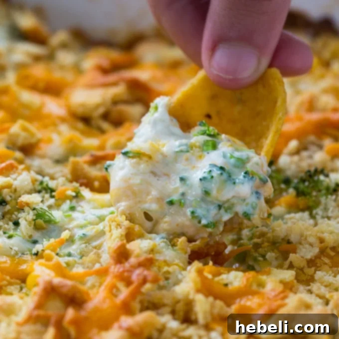 Warm, Gooey Broccoli Cheese Dip with a golden cracker topping, served with Frito chips and baguette slices, perfect for scooping.
