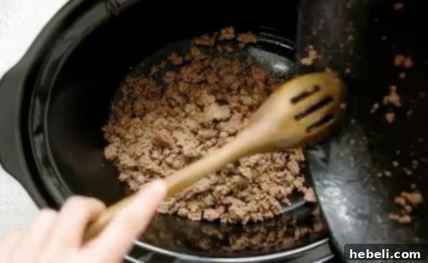 Ground beef being transferred to slow cooker for dip
