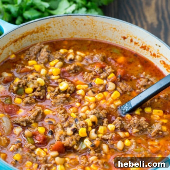 A steaming bowl of Black-Eyed Pea and Sausage Chili, garnished with fresh herbs.